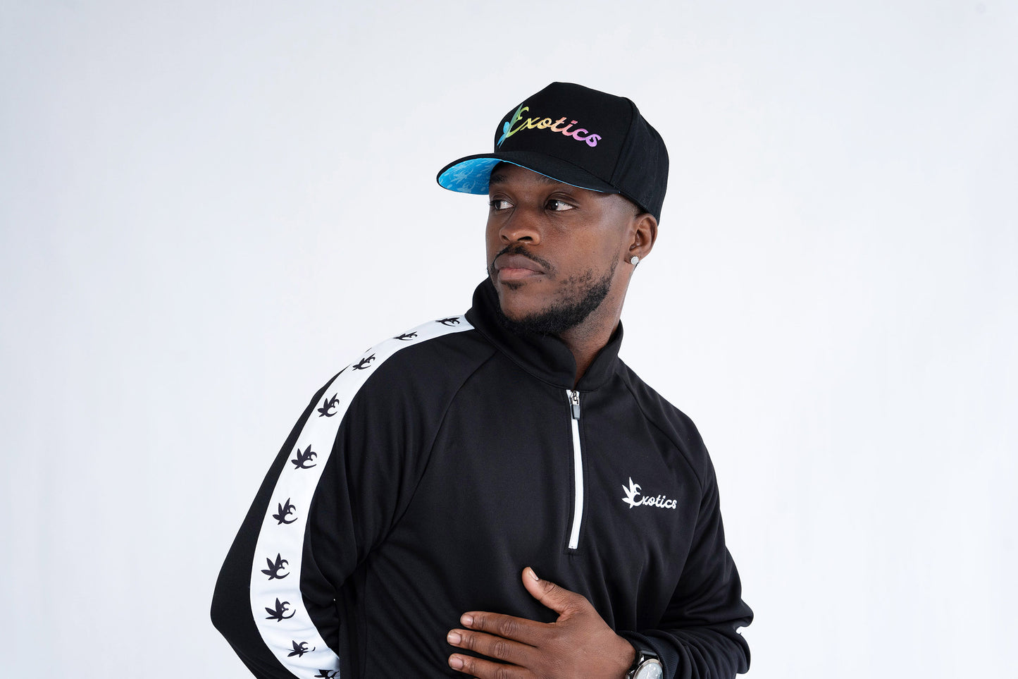 Man wearing black Exotics rainbow logo snapback hat and black tracksuit