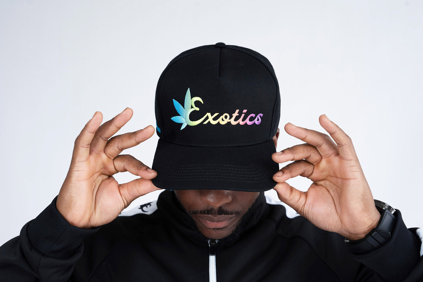 Man wearing black Exotics snapback hat with embroidered rainbow logo