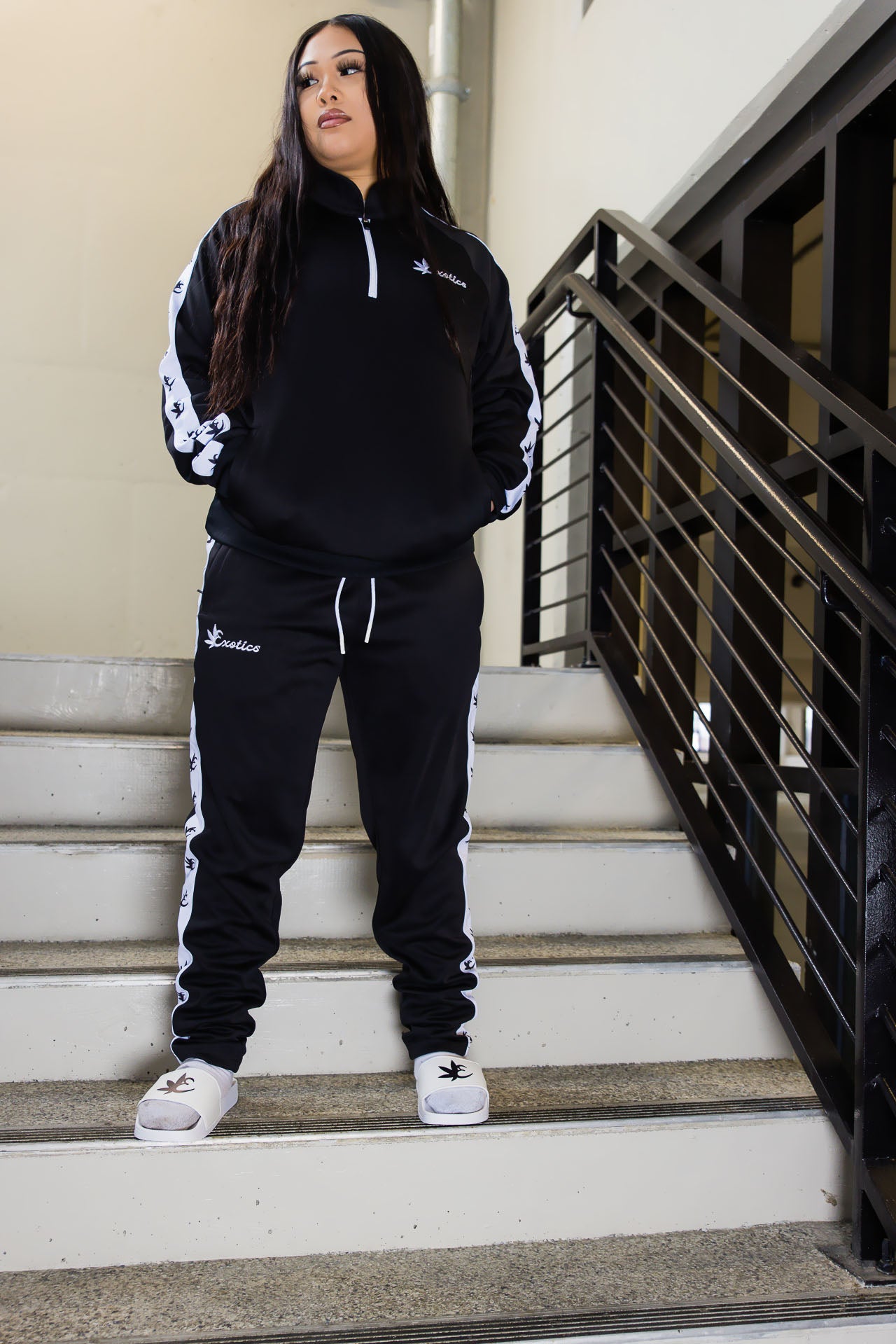 Woman wearing black Exotics tracksuit and white slides in stairwell
