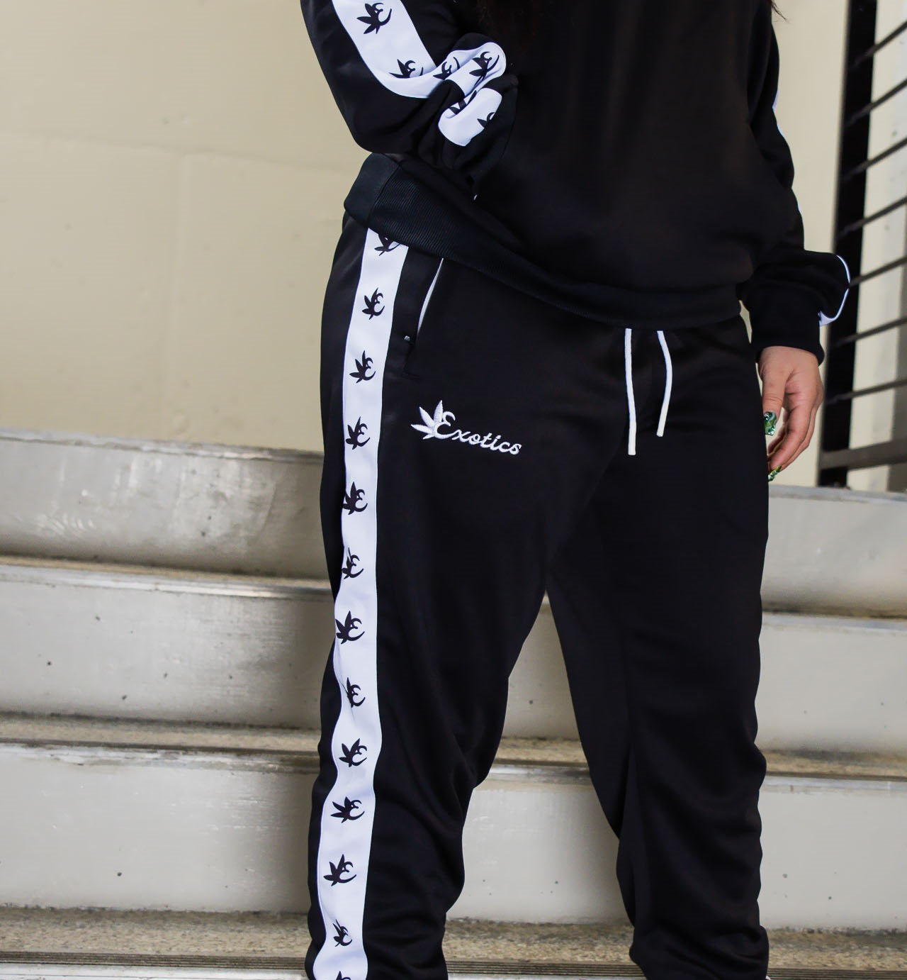 Woman wearing black Exotics tracksuit with white logo and details in stairwell