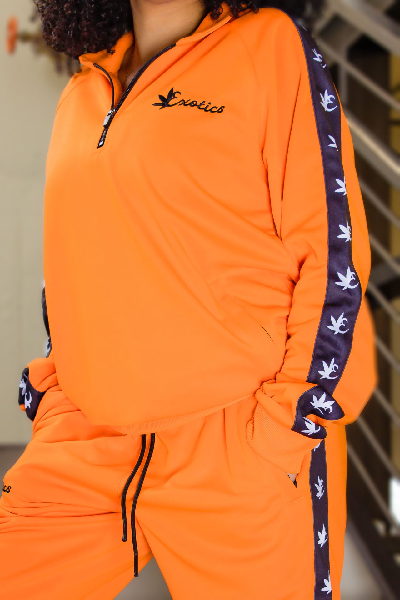 Woman wearing orange Exotics tracksuit with black logo and details