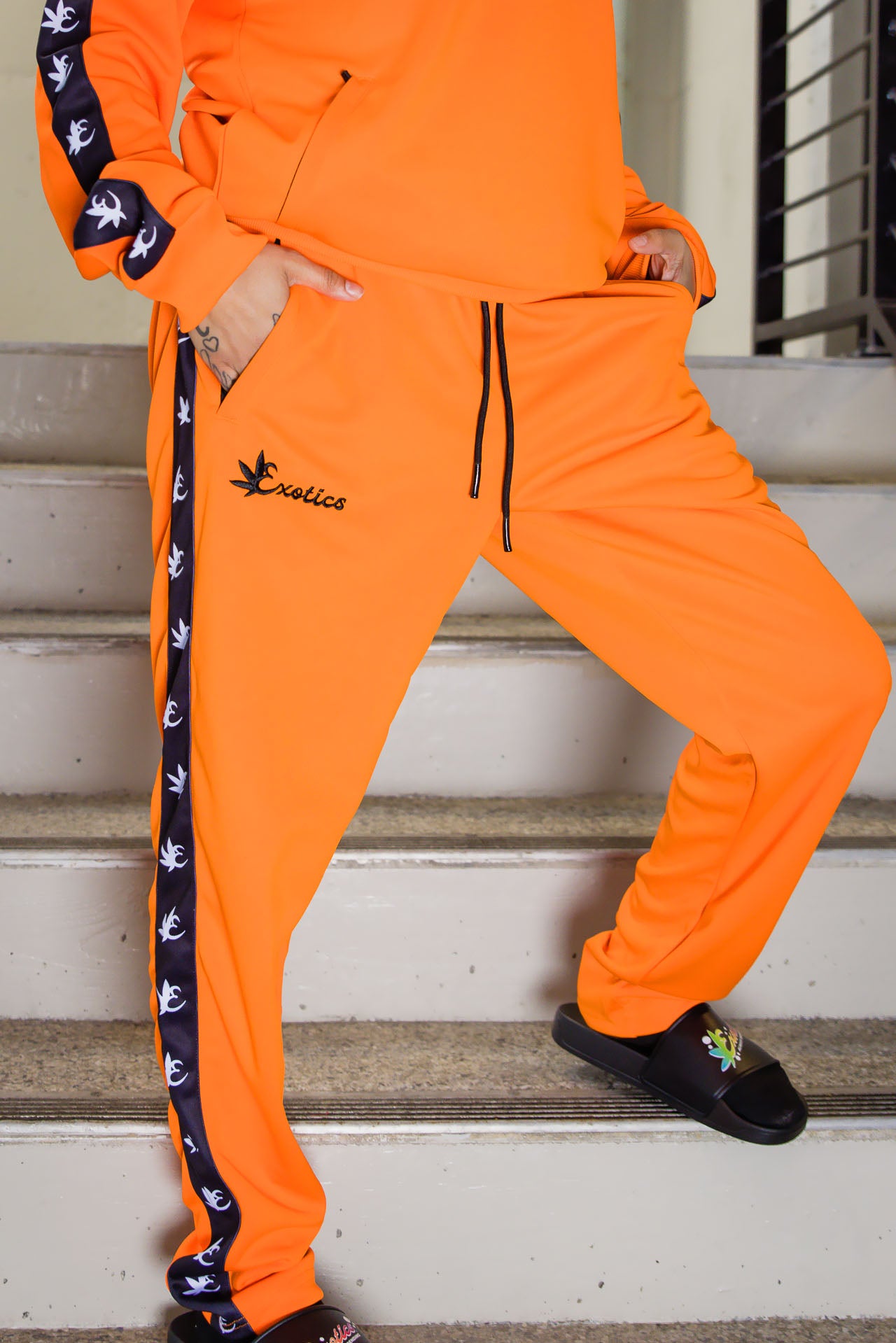 Orange Exotics tracksuit and black slides in stairwell