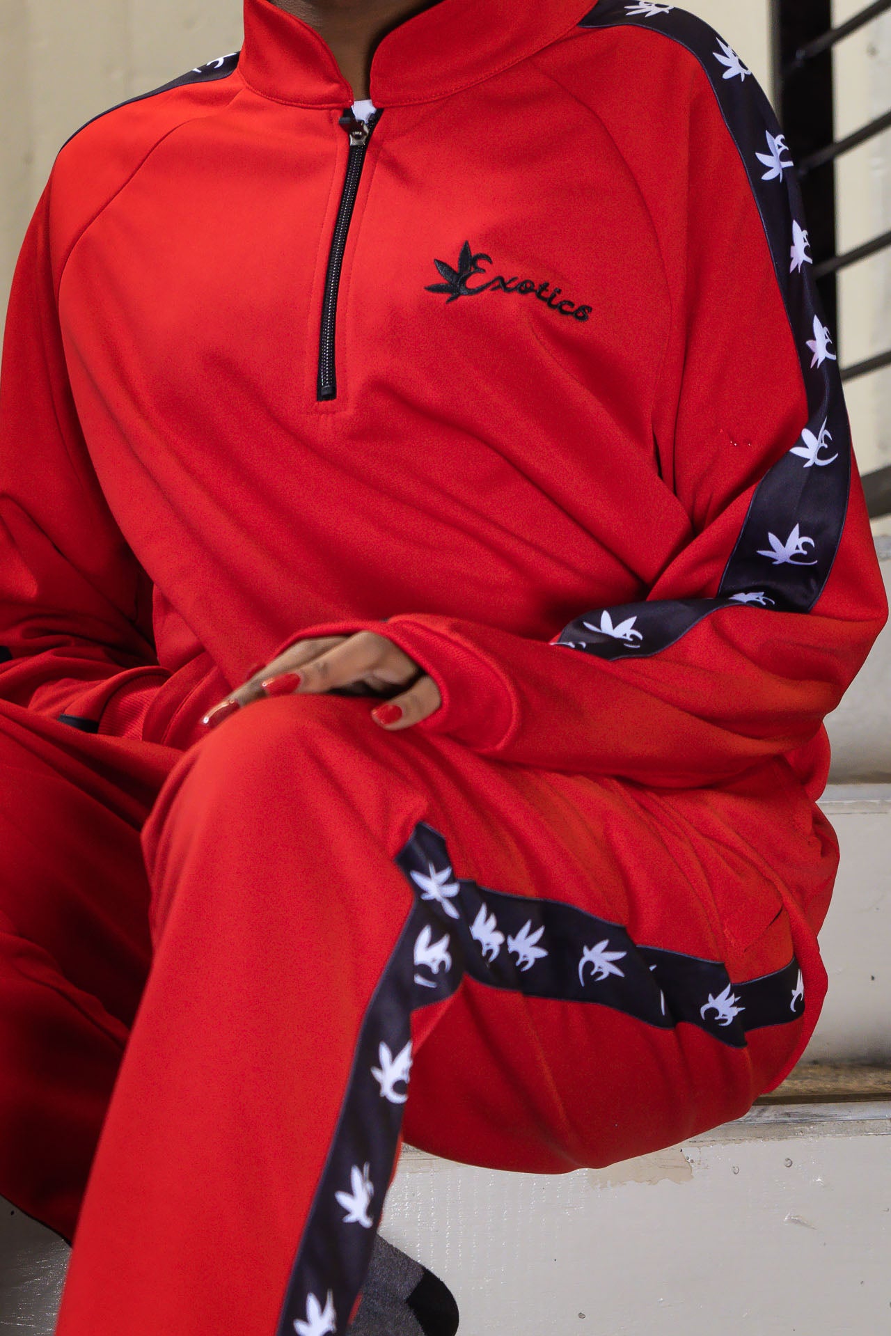 Seated woman wearing red Exotics tracksuit with black logo and details